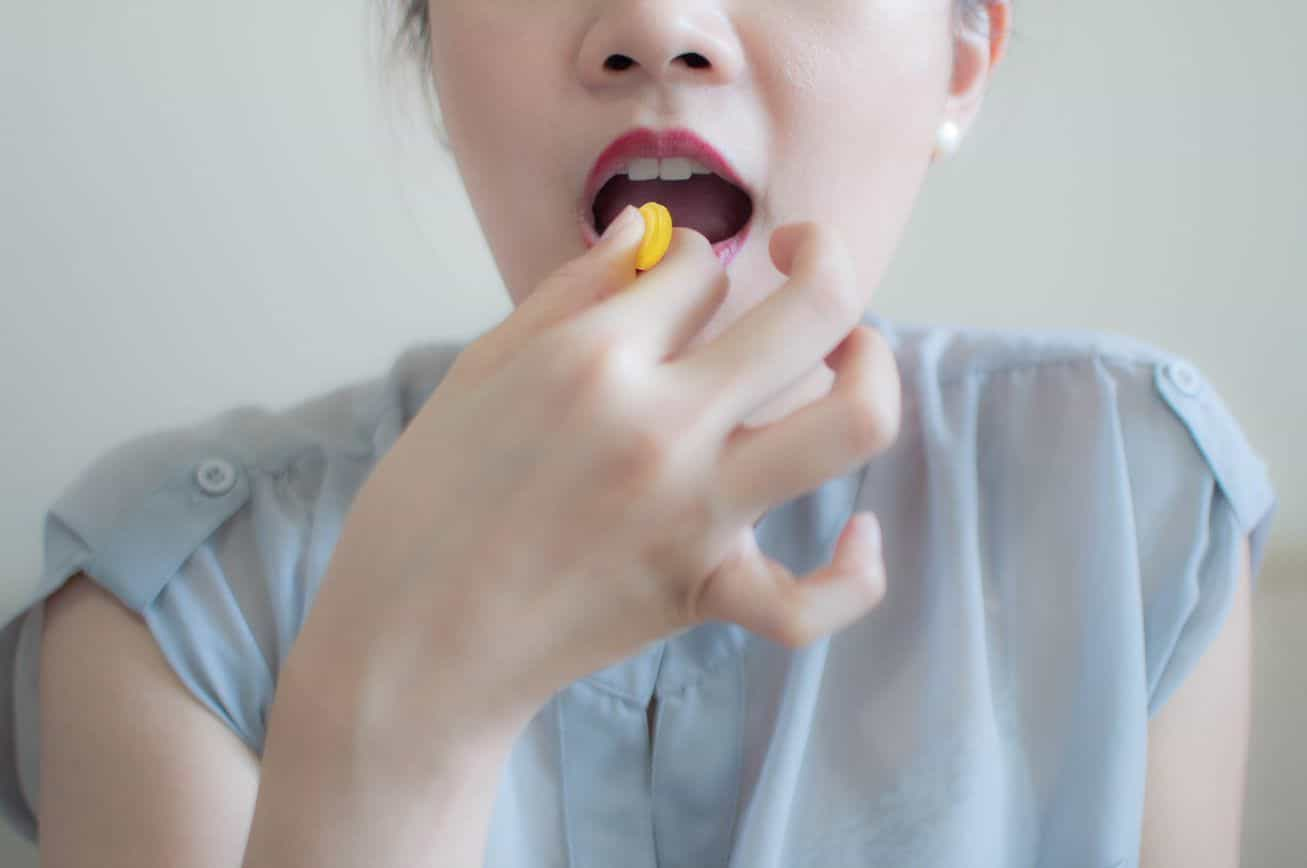 Mujer tomando pastilla para la garganta